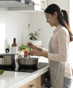 Vietnamese woman cooking with induction stove and modern cookware set, clean kitchen, steam rising from pot, Vietnamese labels on stove buttons